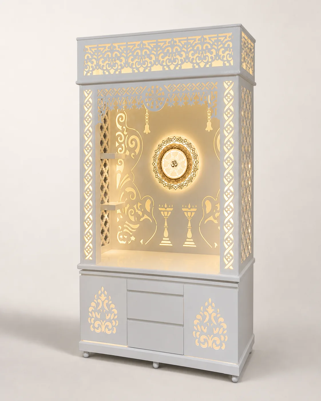 Tall white mandir unit with scrollwork pediment, backlit Om wheel medallion and carved jaali side panels.